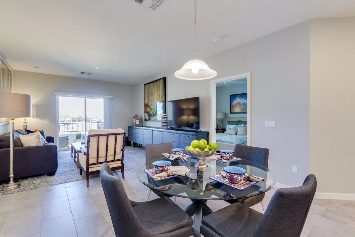 A bright, open social space with a dining table adorned with a fruit centerpiece, comfortable seating, a large TV, and stylish artwork. The room exudes warmth and sociability, ideal for gatherings, entertaining, or working remotely.