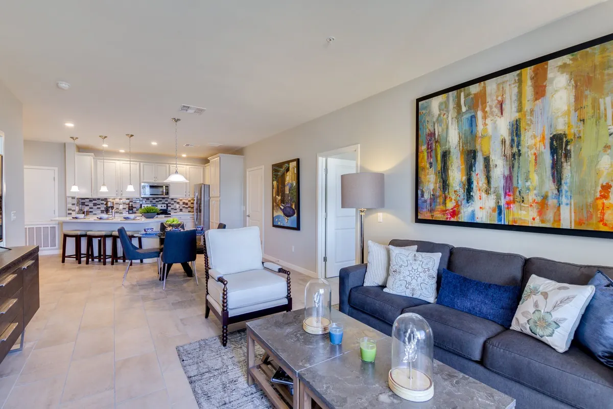 The open-plan living and dining area has a comfortable, contemporary sofa positioned near a stylish dining table. Modern abstract art brings a splash of color to the space, and the arrangement invites both relaxing and socializing.