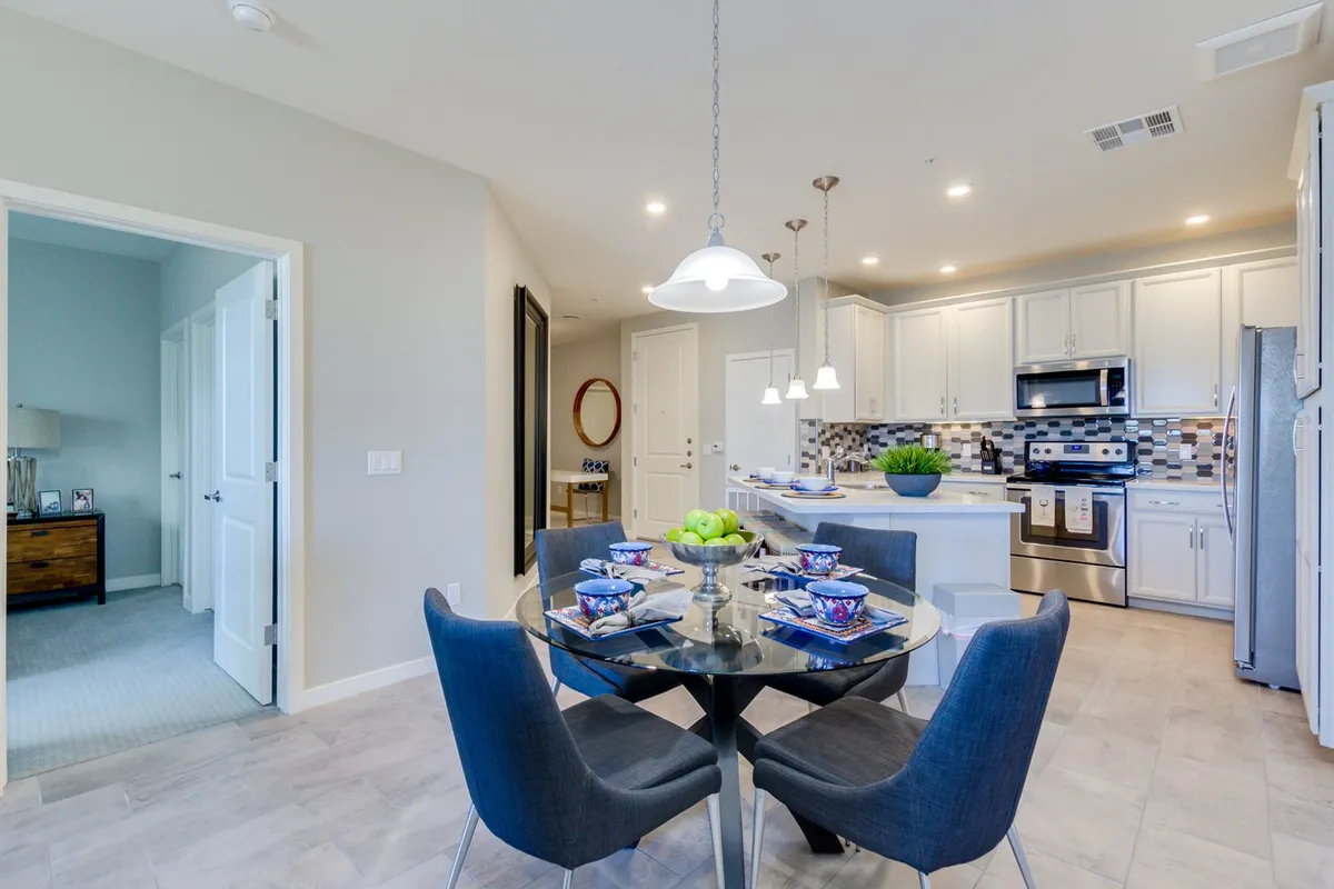 A modern dining area with a beautifully set table, adjacent to a sleek kitchen island and modern appliances. A decorative bowl of apples adds a welcoming touch, and the space invites both family meals and group entertaining.