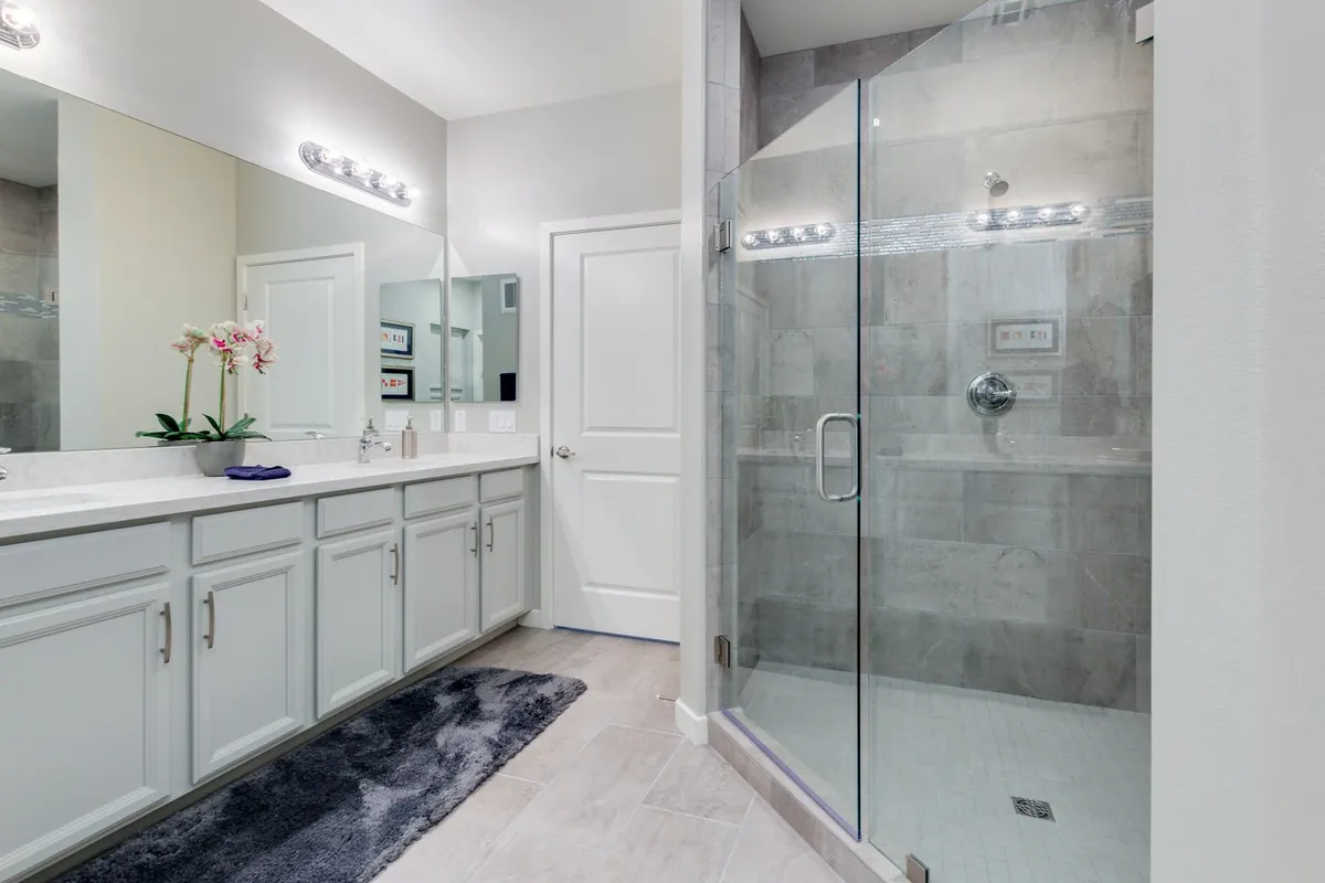 A spa-inspired bathroom with a double sink vanity, expansive mirrors, a glass shower enclosure, and a delicate decorative orchid. The elegant, tranquil atmosphere is enhanced by thoughtful details and abundant space for personal routines.
