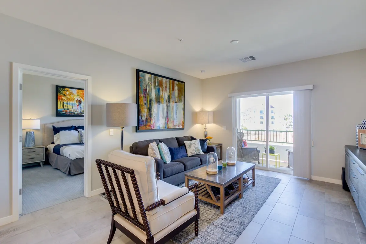 A sunlit living area with a comfortable sofa, colorful abstract artwork, a stylish coffee table, and a large window that floods the space with natural light. The scene feels open and connected to the city, perfect for relaxing after an urban outing or preparing for a day of work and exploration.