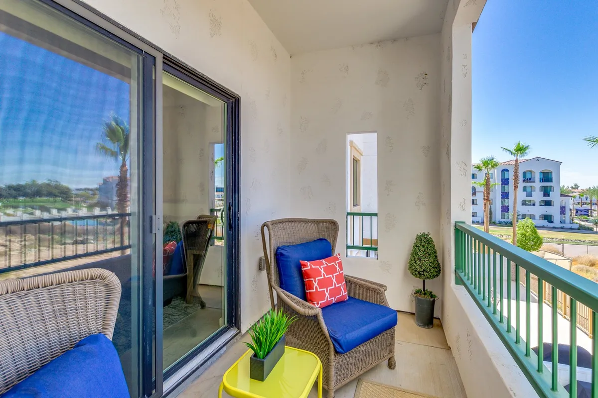 This image captures an inviting exterior seating area featuring comfortable wicker chairs with colorful cushions, a small potted plant, and a green railing. The setup is perfect for relaxing outdoors, enjoying morning coffee, or unwinding after a day on the golf course.