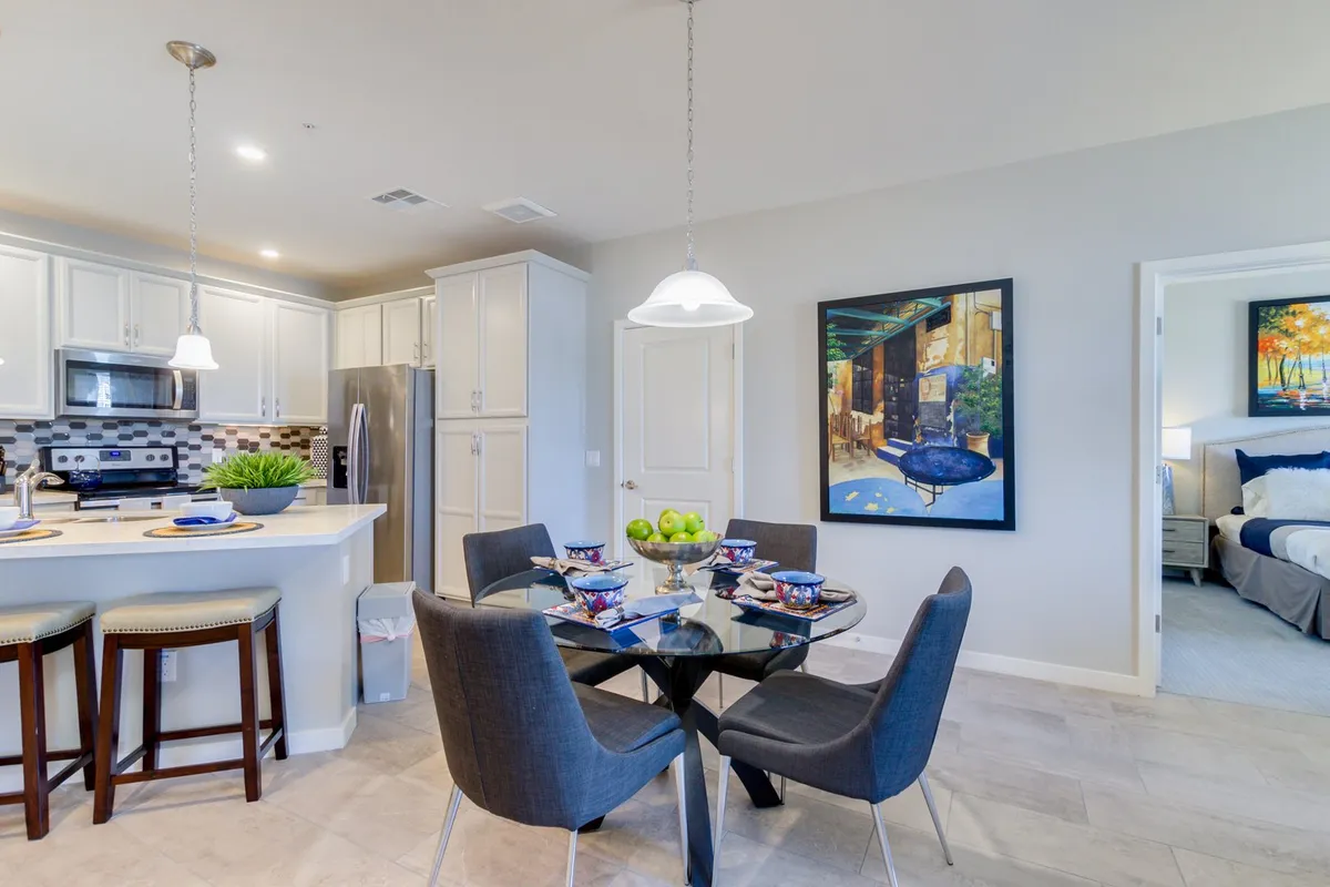 A stylish dining area with a glass table, vibrant artwork, and stainless steel appliances in view. The setup is ideal for both intimate meals and larger gatherings, enhanced by the lively décor.