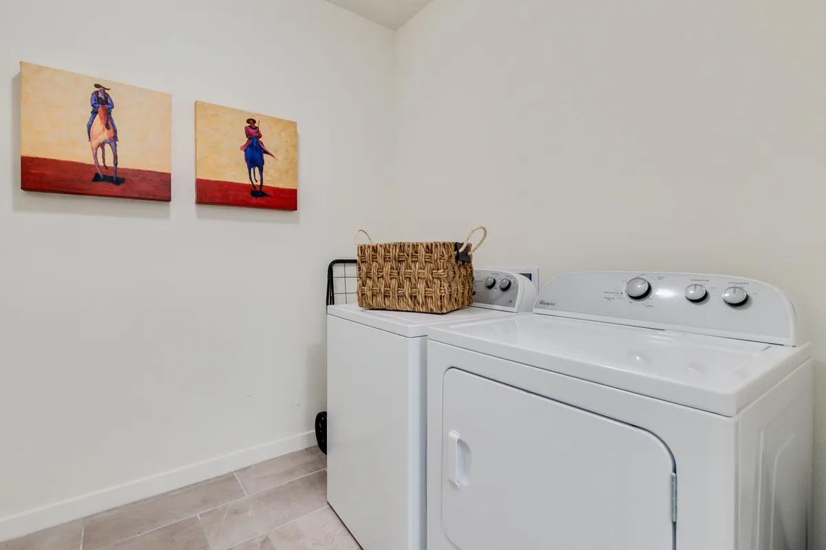A functional laundry area equipped with a washing machine and dryer, complemented by a stylish wall artwork and a woven basket for laundry. The design merges utility with subtle artistic touches, making daily chores feel less mundane.