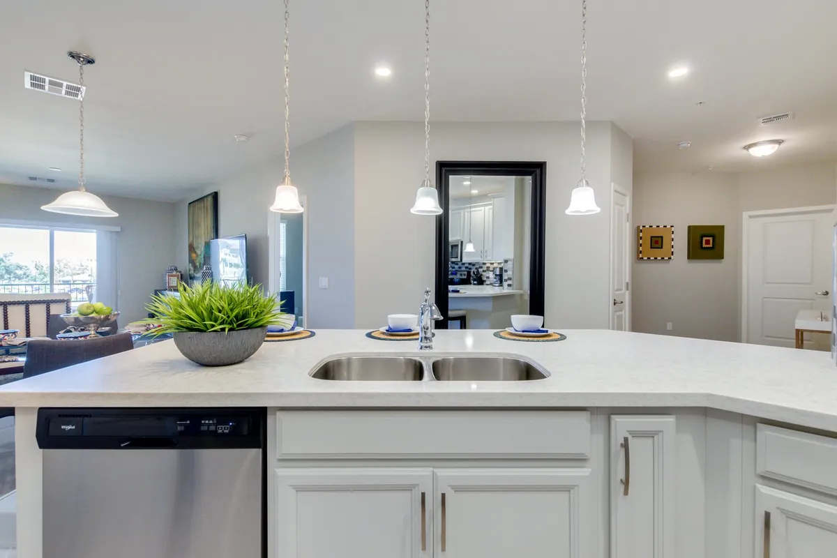 A wide view of an inviting kitchen island with pendant lights, a decorative plant, and a dining area in the background. The scene is set for cooking, entertaining, and family gatherings, with plenty of natural light and a warm, welcoming feeling.